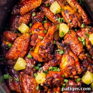 A crockpot packed with pineapple brown sugar soy sauce Hawaiian wings. The chicken wings are topped with chunks of pineapple and chopped scallions.