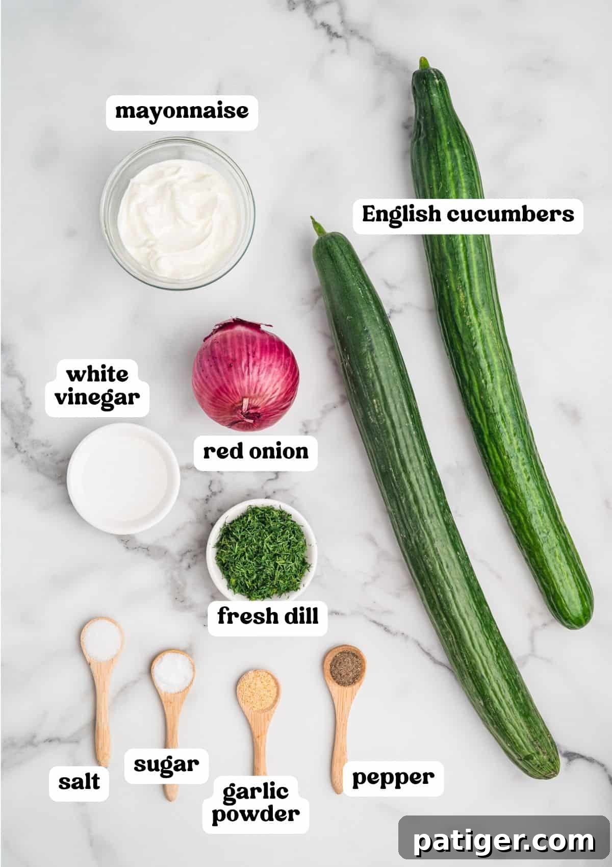 Overhead image of ingredients on a marble surface, each labeled: mayonnaise, white vinegar, red onion, fresh dill, salt, sugar, garlic powder, pepper, and two English cucumbers.