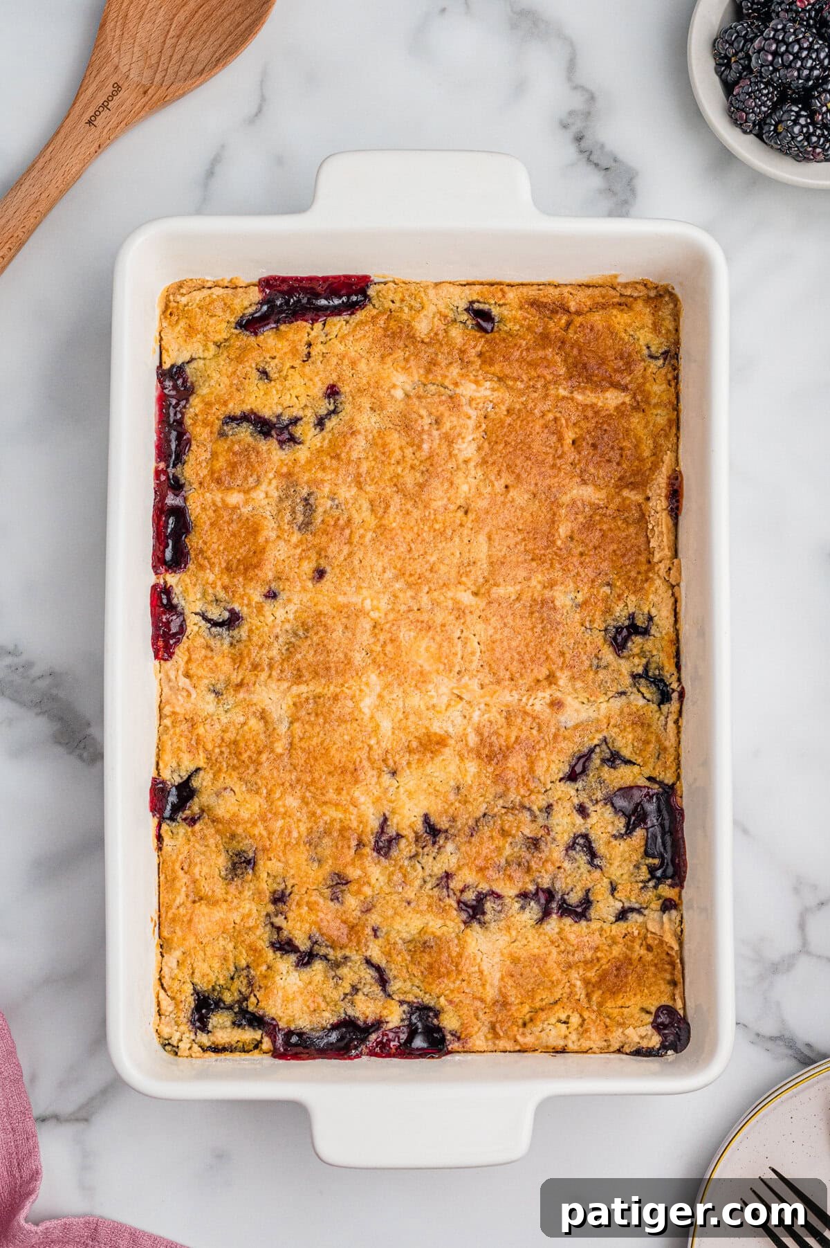 Freshly baked blackberry dump cake in a 9x13 inch baking dish, featuring a beautiful golden-brown, crumbly top with hints of dark purple berry filling bubbling up around the edges.