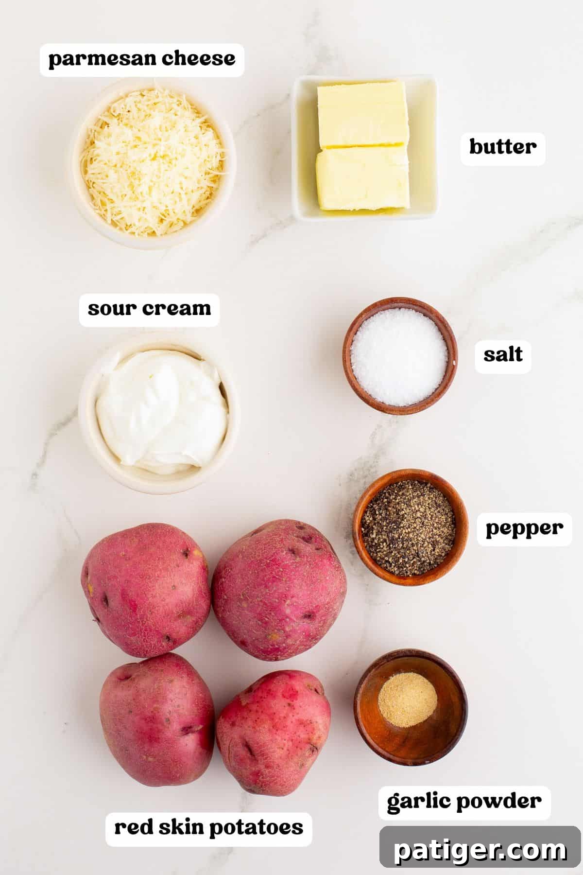 Rustic Red Potato Mash 3 Overhead view of ingredients for mashed red potatoes with labels: Parmesan cheese, butter, sour cream, salt, pepper, garlic powder, and four whole red skin potatoes.