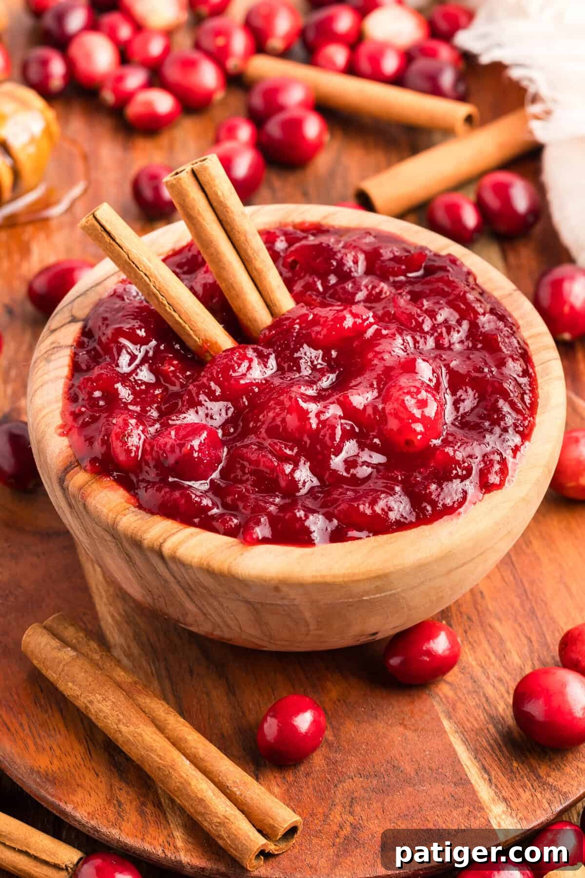 Overhead view of homemade cranberry sauce in a wooden bowl with whole cranberries cinnamon sticks.