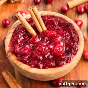 Homemade cranberry sauce in a wooden bowl with whole cranberries cinnamon sticks.
