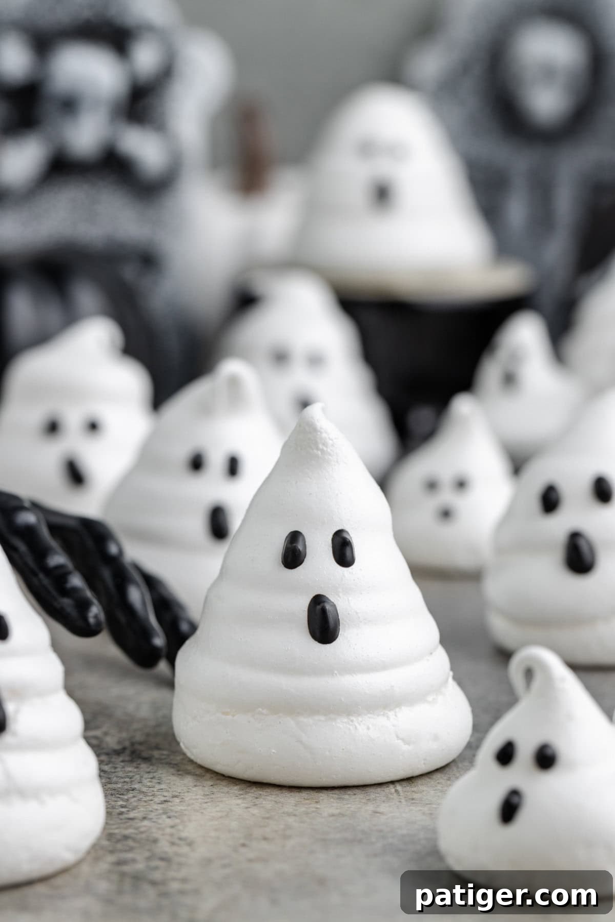 Ghost meringue cookie in foreground with a black gloved hand reaching toward it.Ghost meringue in foreground with a black gloved hand reaching toward it. More ghost meringues are blurred in the background.