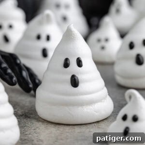 Ghost meringue cookie with a black gloved hand reaching toward it.Ghost meringue in foreground with a black gloved hand reaching toward it. More ghost meringues are in the background.