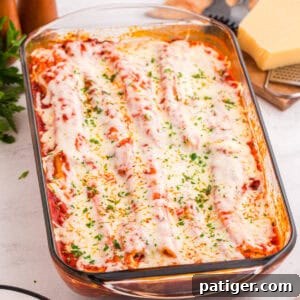 Baked manicotti covered in tomato sauce, melted mozzarella cheese, and garnished with chopped parsley in a glass baking dish. The cheese is slightly browned and bubbly on top.