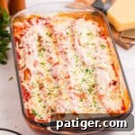 Baked manicotti covered in tomato sauce, melted mozzarella cheese, and garnished with chopped parsley in a glass baking dish. The cheese is slightly browned and bubbly on top.