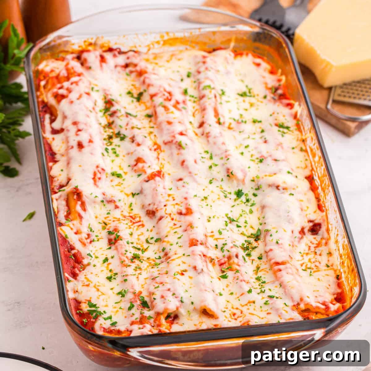 Baked manicotti covered in tomato sauce, melted mozzarella cheese, and garnished with chopped parsley in a glass baking dish. The cheese is slightly browned and bubbly on top.