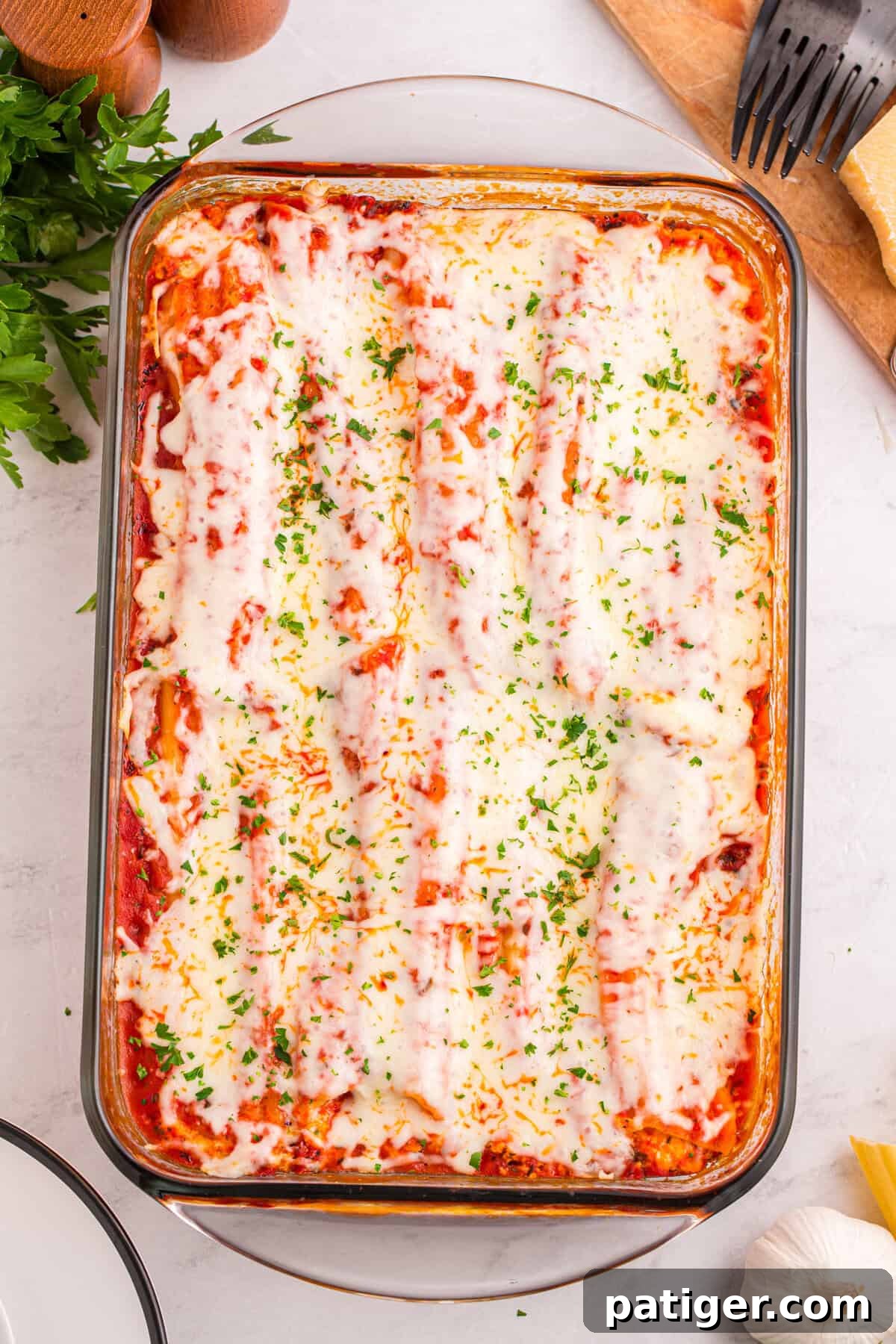 Overhead shot of a glass baking dish filled with neatly arranged manicotti covered in melted mozzarella and tomato sauce, garnished with chopped parsley.