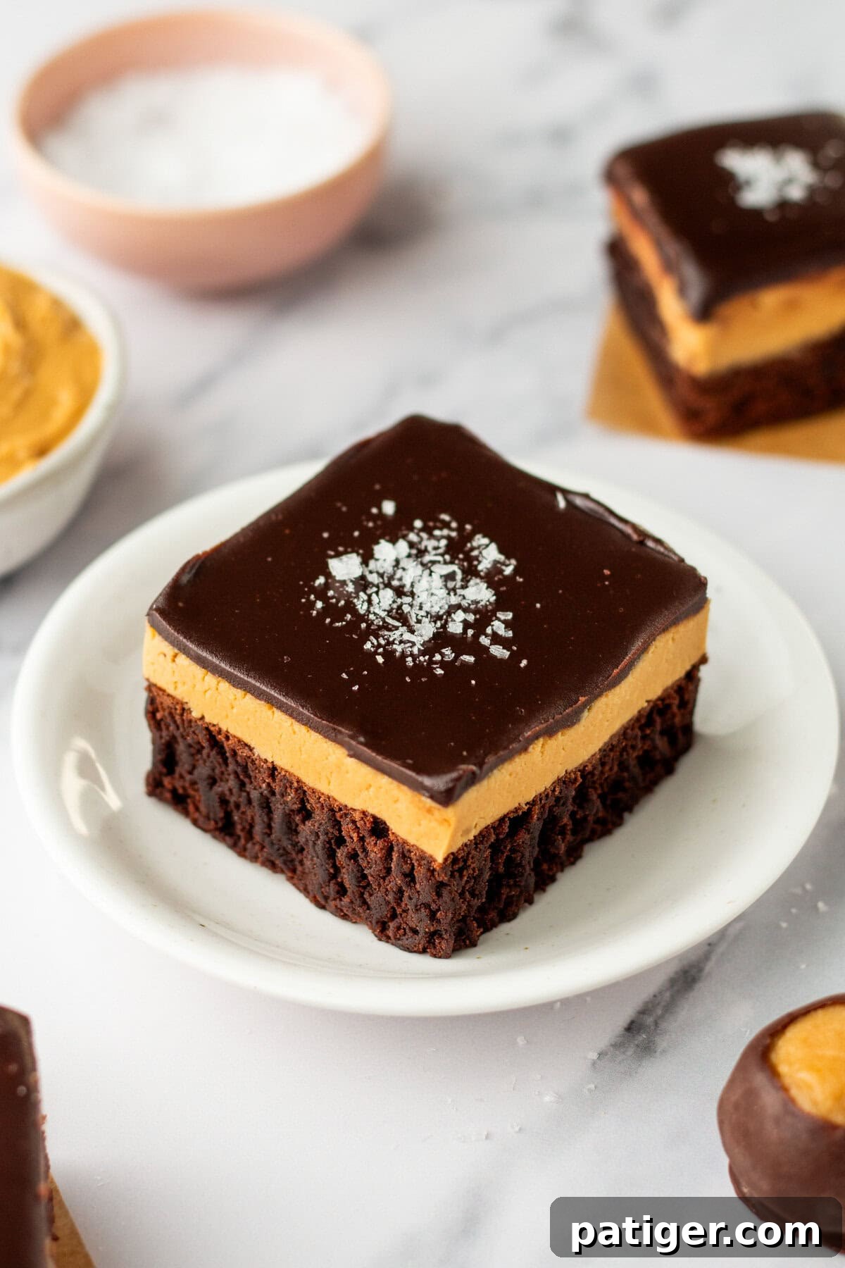 Decadent Buckeye Brownies 2 A buckeye brownie with three layers: a chocolate brownie base, a thick peanut butter layer, and a smooth chocolate ganache topping sprinkled with flaky sea salt.