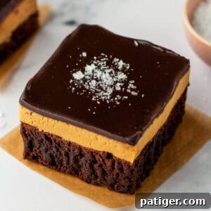 A buckeye brownie with three layers: a chocolate brownie base, a thick peanut butter layer, and a smooth chocolate ganache topping sprinkled with flaky sea salt.
