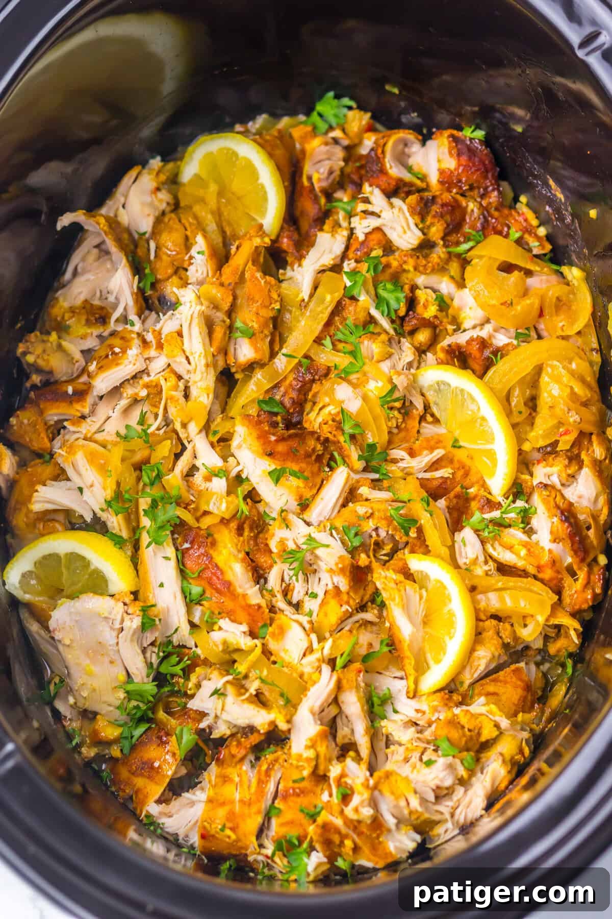 Melt-in-Your-Mouth Slow Cooker Chicken Shawarma 3 Crockpot chicken shawarma, featuring marinated shredded chicken, onions, lemon wedges, and garnished with chopped parsley.