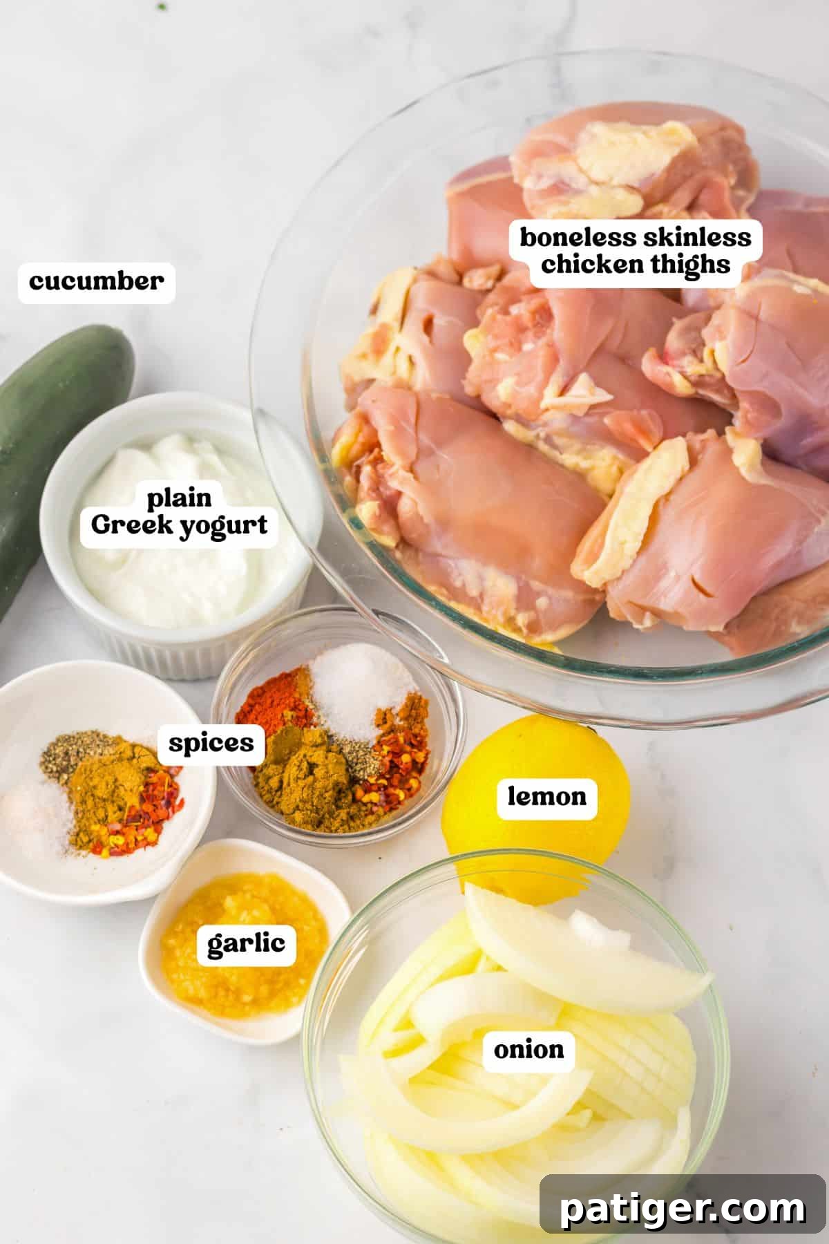 Melt-in-Your-Mouth Slow Cooker Chicken Shawarma 4 Raw ingredients labeled for chicken shawarma, including boneless skinless chicken thighs in a glass bowl, sliced onion, lemon, minced garlic, various spices in small bowls, plain Greek yogurt, and a whole cucumber.