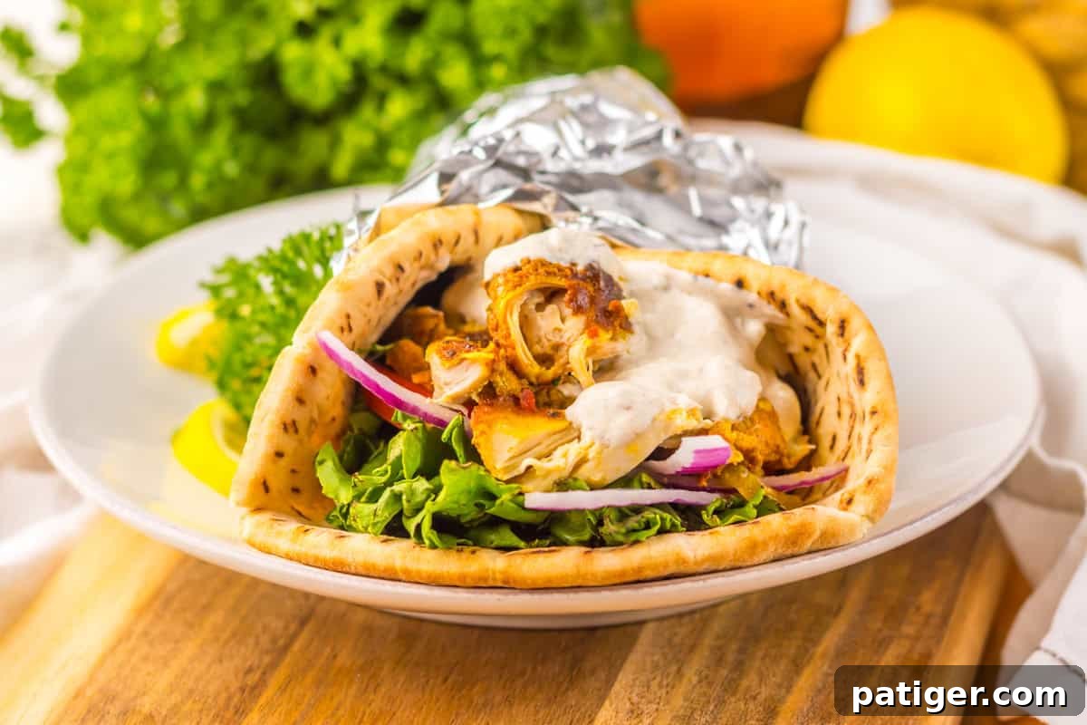 Melt-in-Your-Mouth Slow Cooker Chicken Shawarma 8 A pita wrap stuffed with shredded chicken, lettuce, tomato, red onion, and white sauce, partially wrapped in foil.