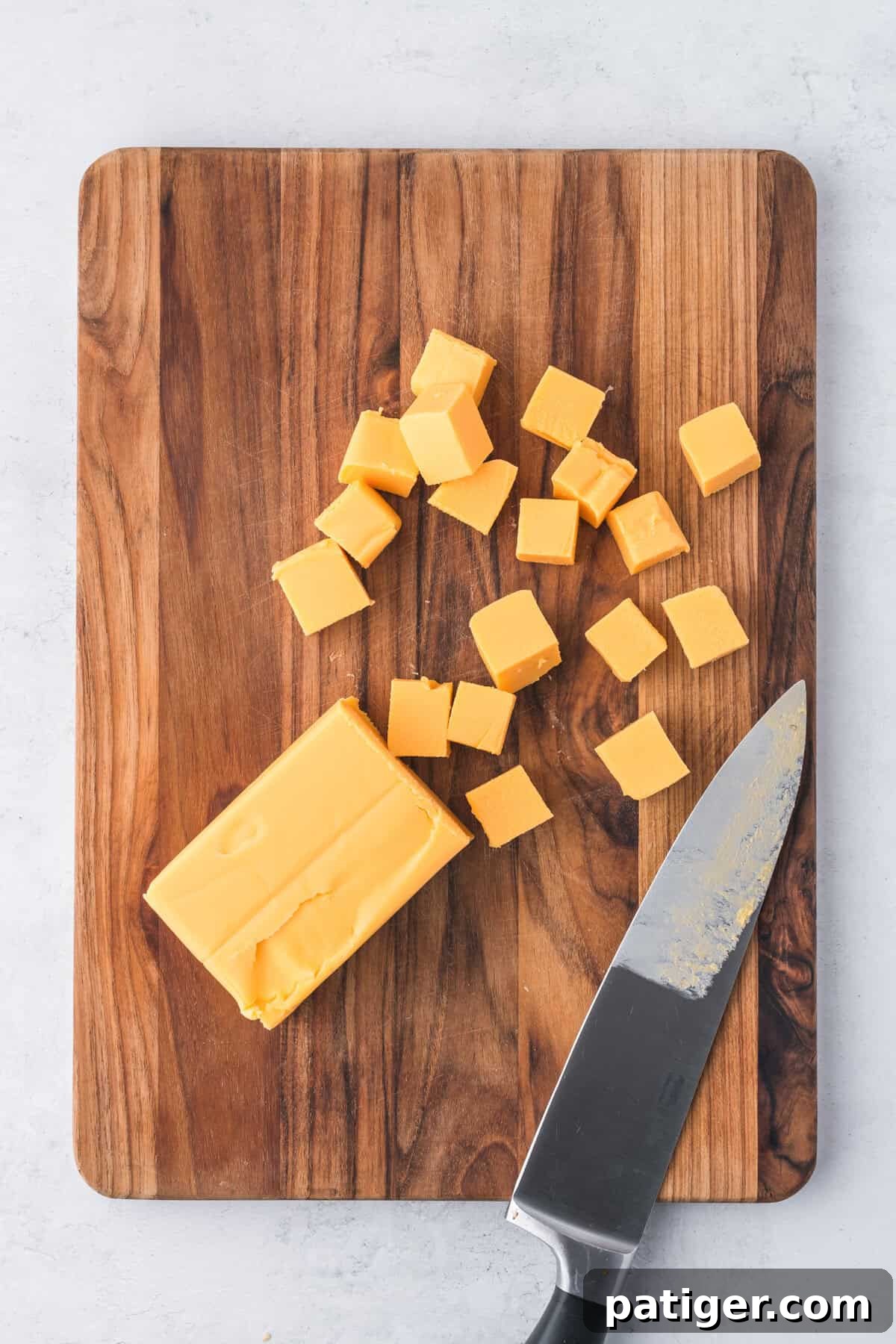 Cubes of Velveeta cheese neatly arranged on a cutting board, next to a full block of Velveeta and a sharp knife.