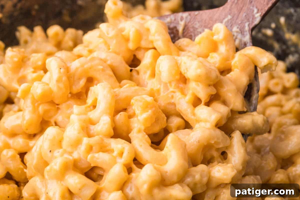 Close-up of irresistibly creamy mac and cheese being scooped with a wooden spoon directly from a slow cooker, showcasing its rich, molten texture.
