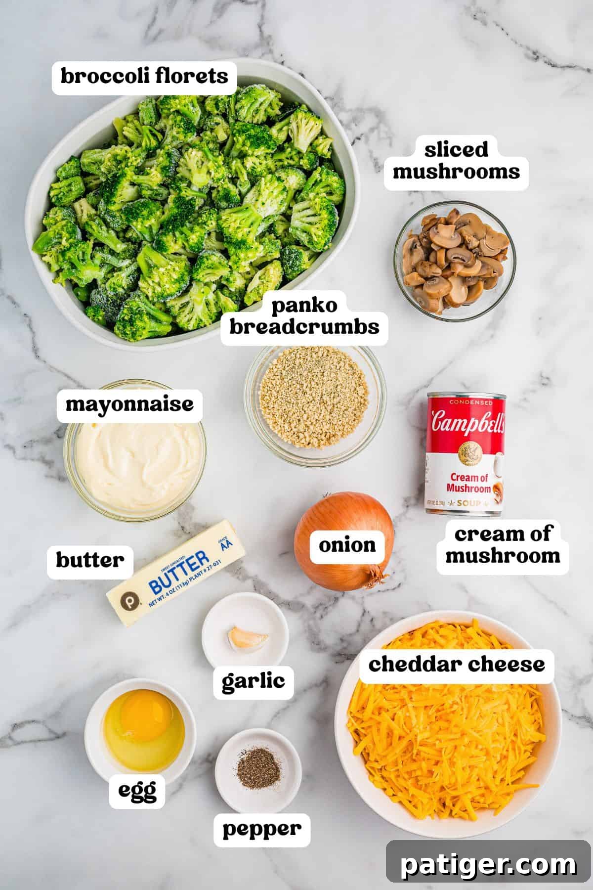 Overhead view of labeled ingredients for broccoli casserole including broccoli florets, sliced mushrooms, panko breadcrumbs, mayonnaise, butter, onion, cream of mushroom soup, garlic, egg, pepper, and shredded cheddar cheese.