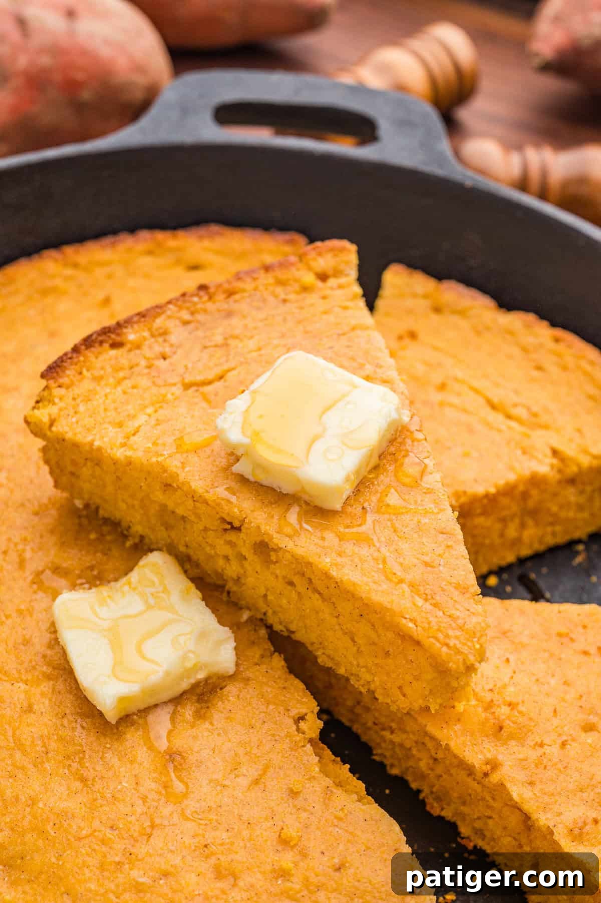 Several slices of sweet potato cornbread in a cast iron skillet with melting butter and honey drizzled on top.