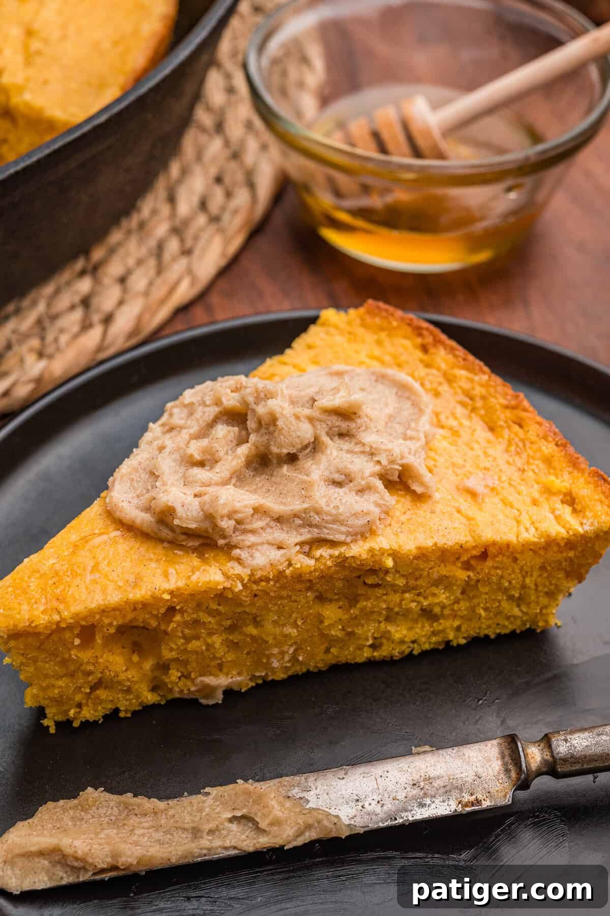 Slice of sweet potato cornbread topped with cinnamon butter spread on a black plate.