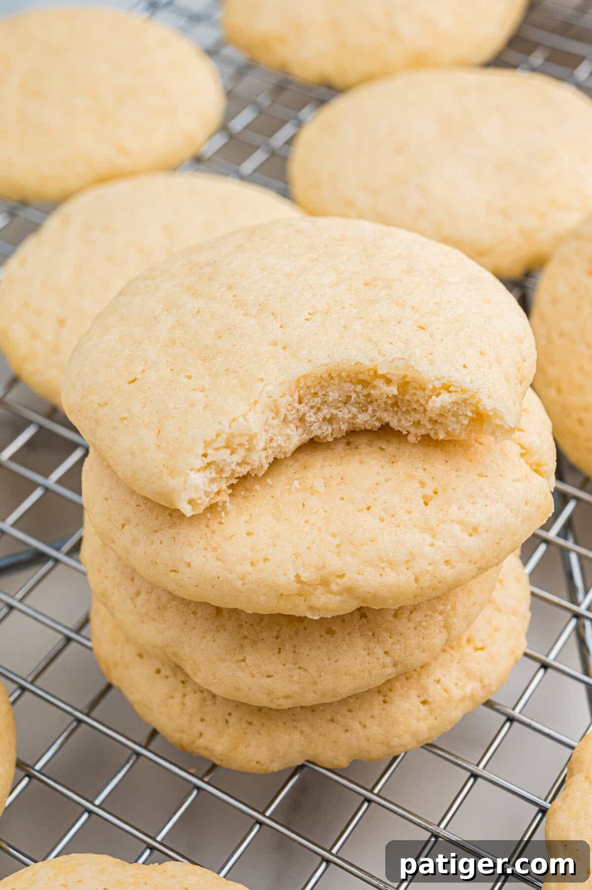 Stack of old-fashioned tea cakes on a wire cooling rack. The top cookie has a visible bite taken from it, revealing its soft, cakey interior.