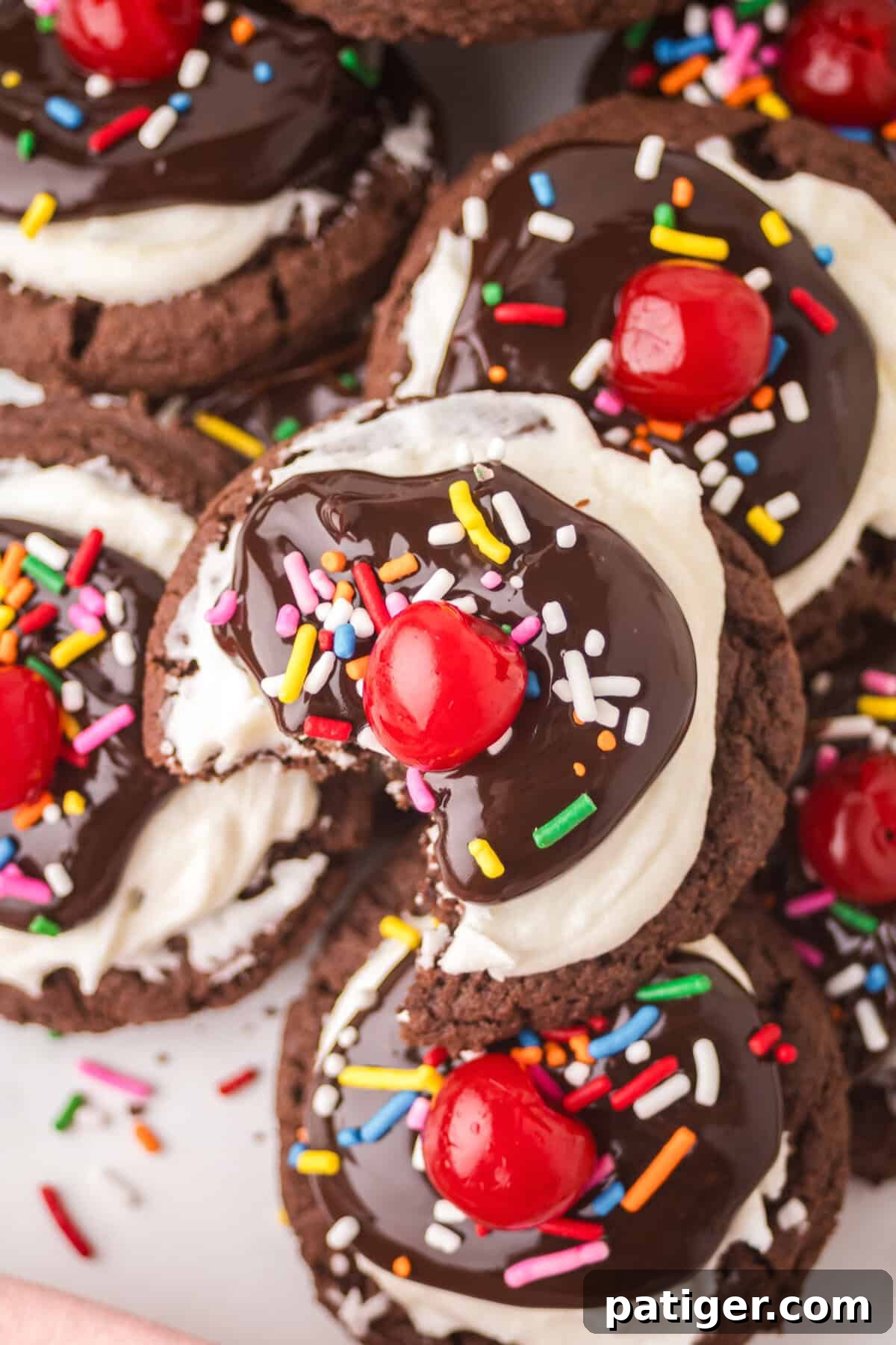 Close-up view of hot fudge sundae cookies, showcasing their intricate toppings, with one cookie having a bite taken out to reveal its soft, fudgy interior.
