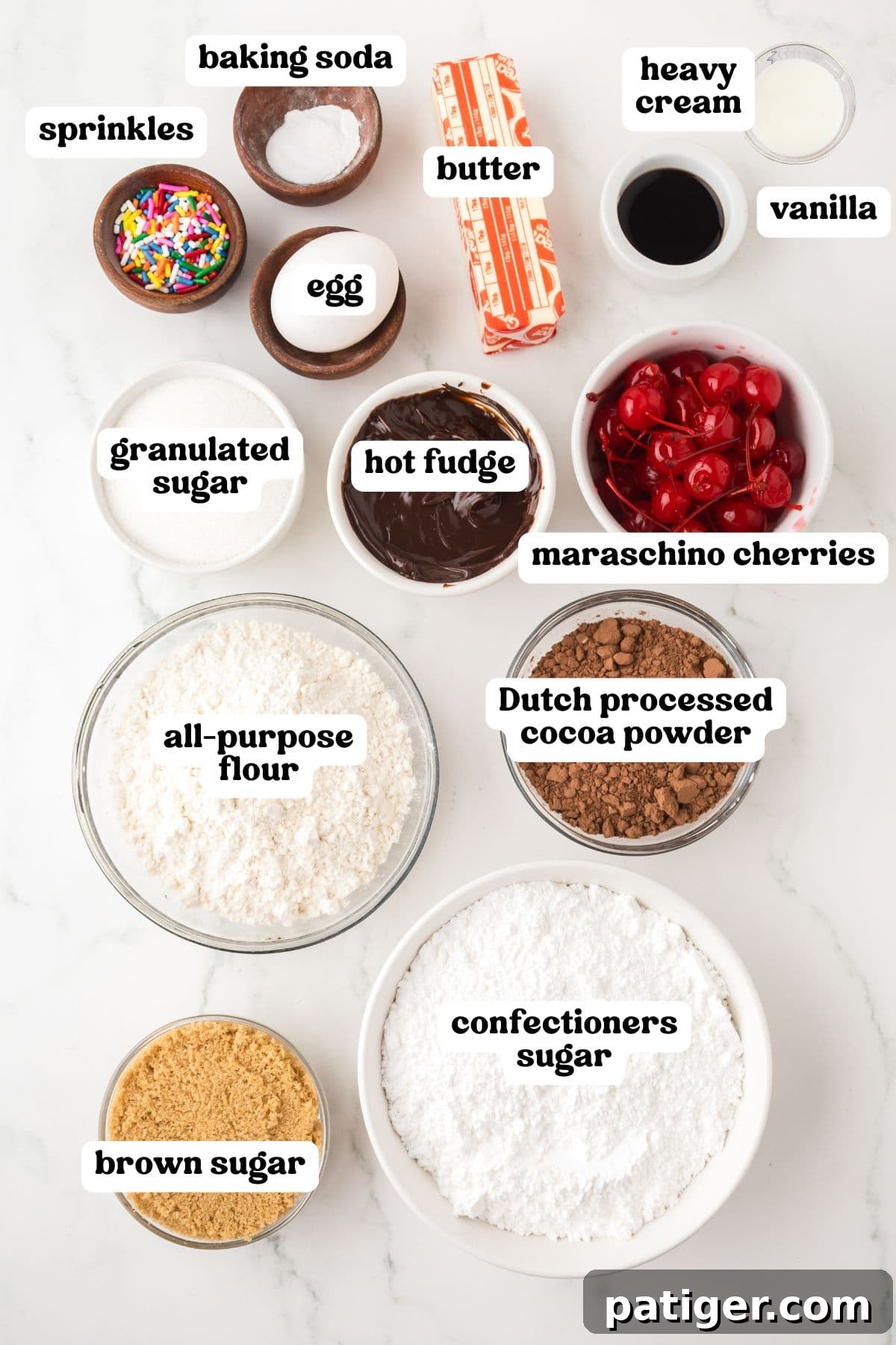 Overhead flat lay of labeled ingredients for Hot Fudge Sundae Cookies, including vibrant rainbow sprinkles, baking soda, soft butter, heavy cream, pure vanilla extract, a large egg, granulated sugar, jarred hot fudge, bright maraschino cherries, all-purpose flour, rich Dutch processed cocoa powder, brown sugar, and fine confectioners sugar.