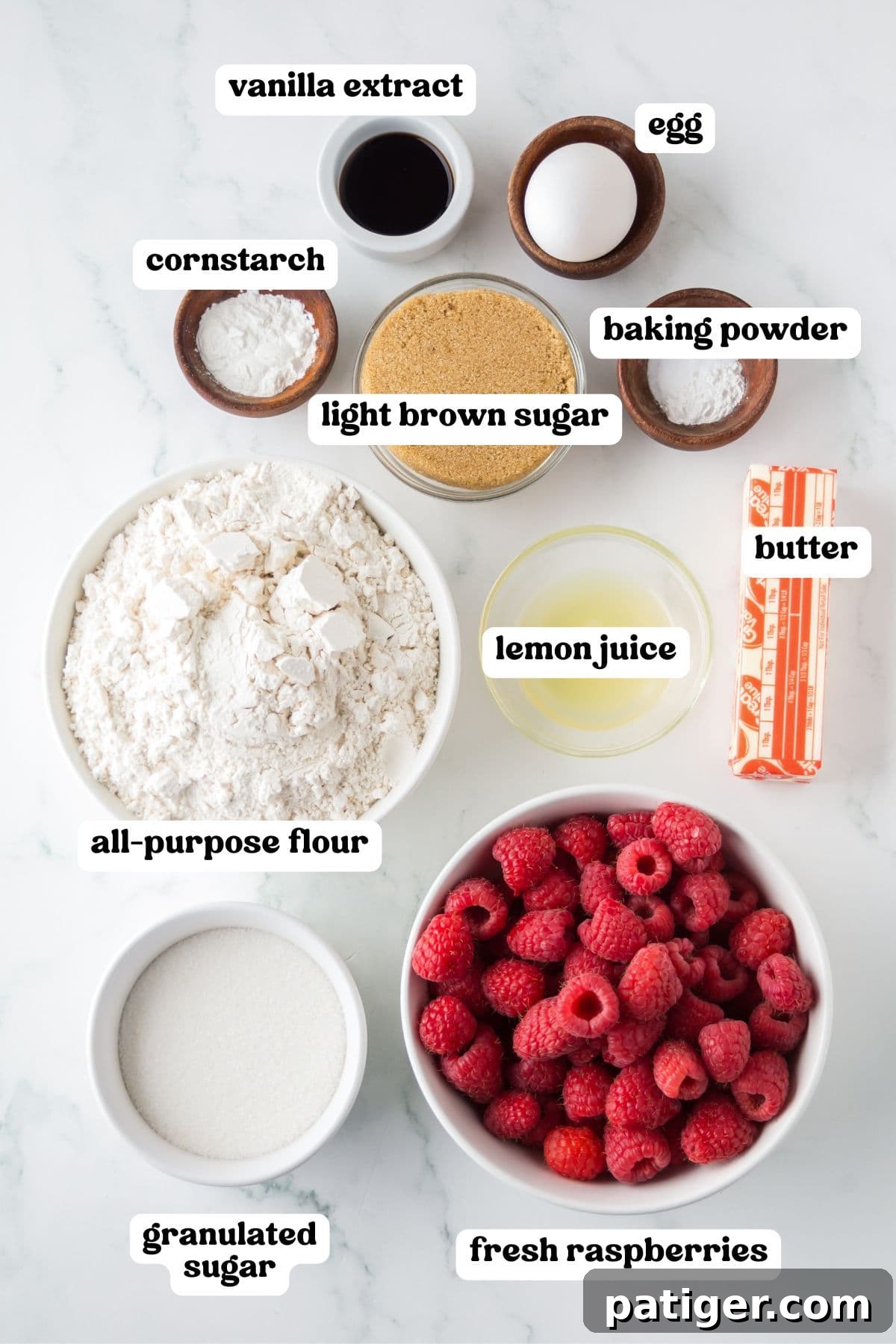 Berry Burst Crumb Bars 4 Flat lay of labeled ingredients for raspberry crumb bars arranged on a white surface, including fresh raspberries, all-purpose flour, granulated sugar, light brown sugar, lemon juice, butter, egg, baking powder, cornstarch, and vanilla extract.