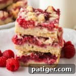 Berry Burst Crumb Bars 9 Stack of three raspberry crumble shortbread bars on a white plate with fresh raspberries.