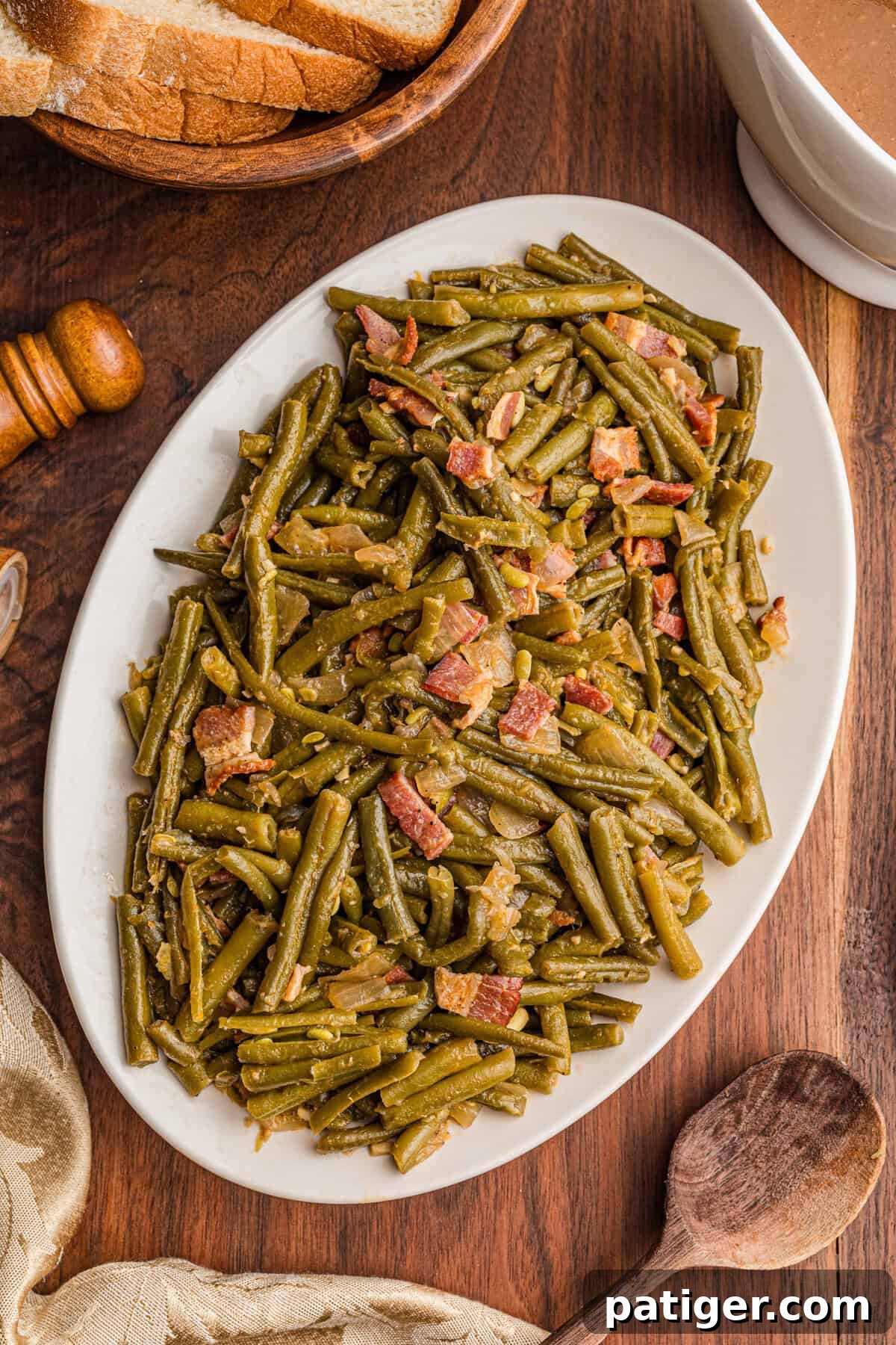 Plate of Southern green beans with bacon next to bread and gravy, showcasing a hearty serving.