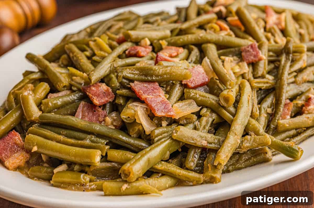 Close-up of cooked Southern-style green beans and bacon served on a white oval plate, highlighting the tender texture.