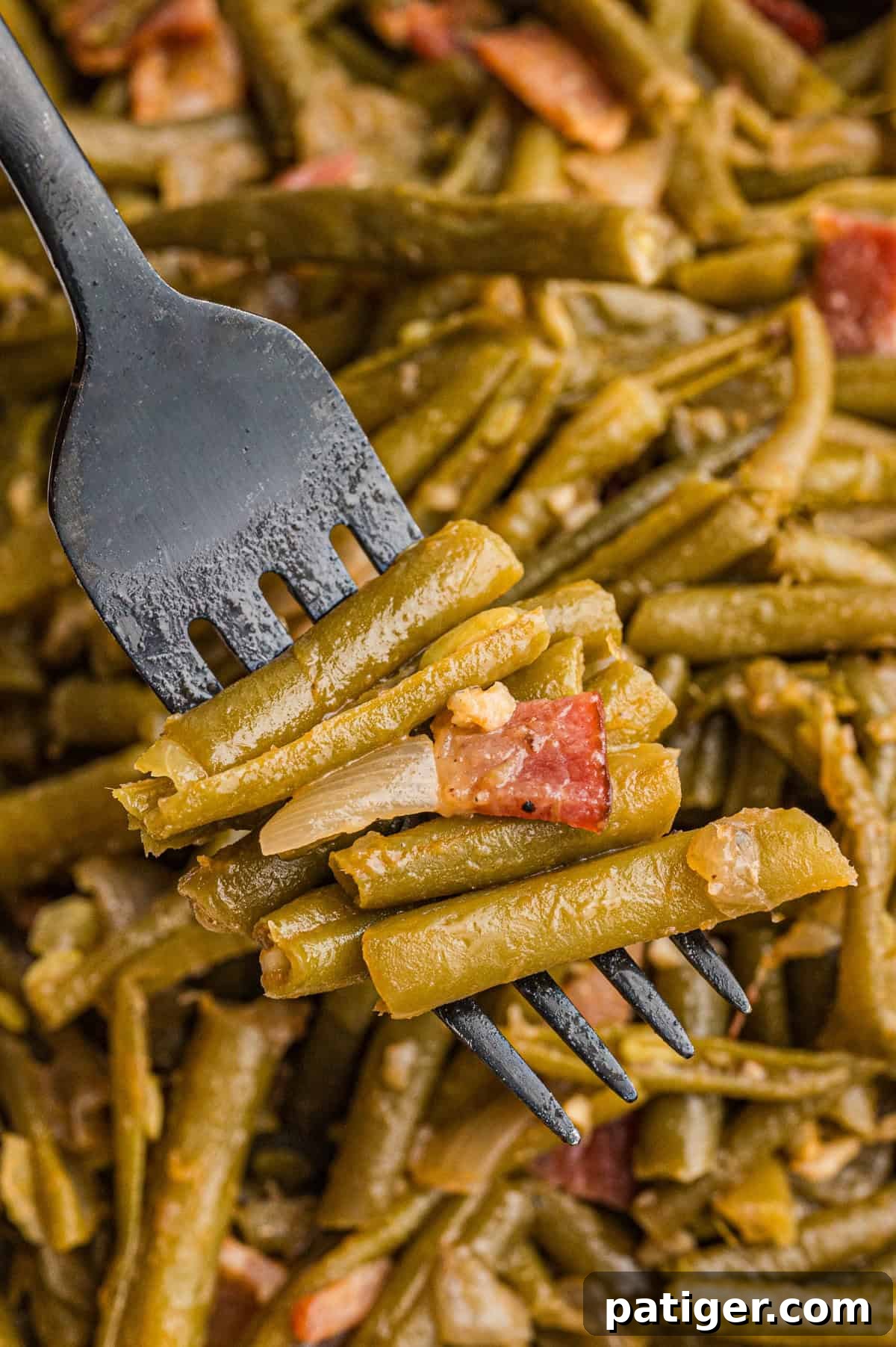 A fork picking up cooked Southern string beans with bacon, onions, and garlic, highlighting the tender texture.