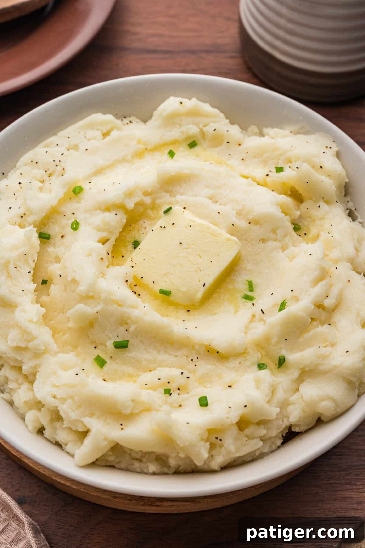 Creamy old-fashioned mashed potatoes in a bowl, topped with a square of butter, melted butter, black pepper, and chopped chives.