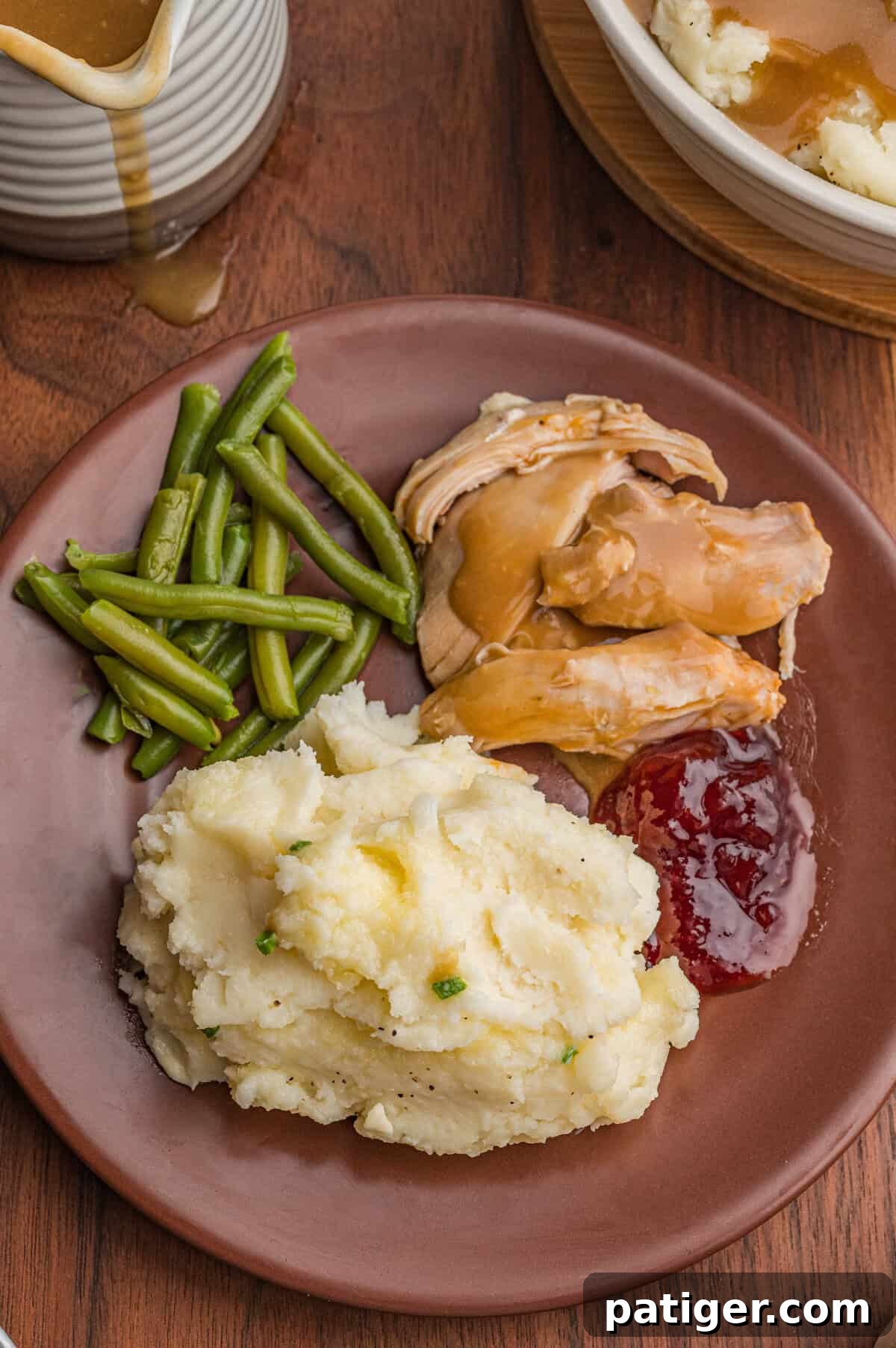 Dinner plate containing mashed potatoes with chives and melted butter, cooked green beans, turkey slices with brown gravy, and cranberry sauce. 
