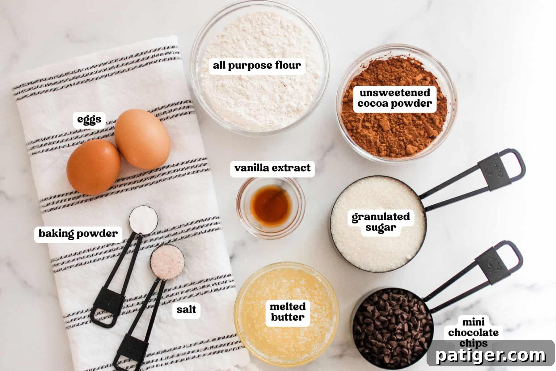 Bite-Sized Brownie Bliss 4 Flat lay of brownie bite ingredients on a white surface with black measuring spoons and a striped towel. Ingredients are labeled: two eggs, baking powder, salt, all-purpose flour, unsweetened cocoa powder, vanilla extract, granulated sugar, melted butter, and mini chocolate chips.