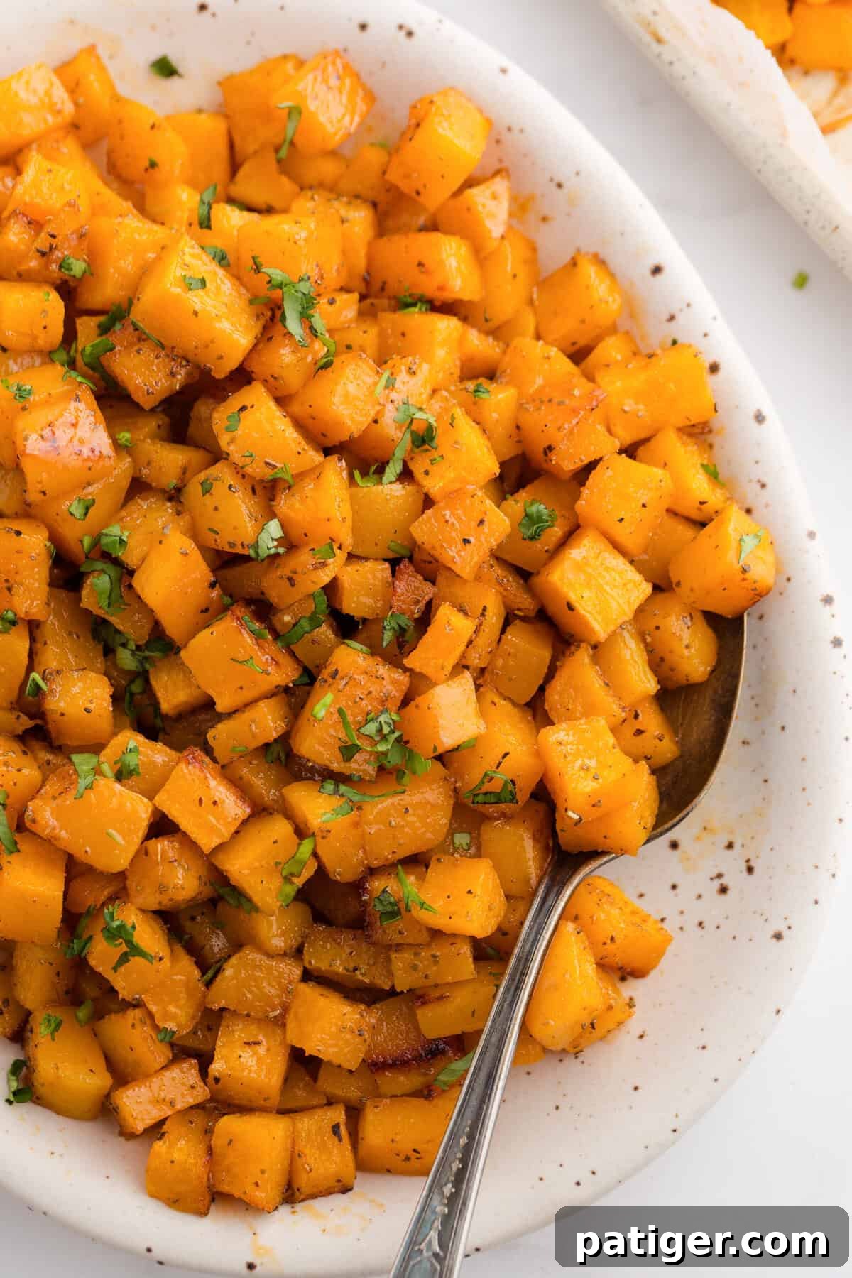 Close-up of roasted butternut squash cubes in a serving dish, glistening with honey and spices.