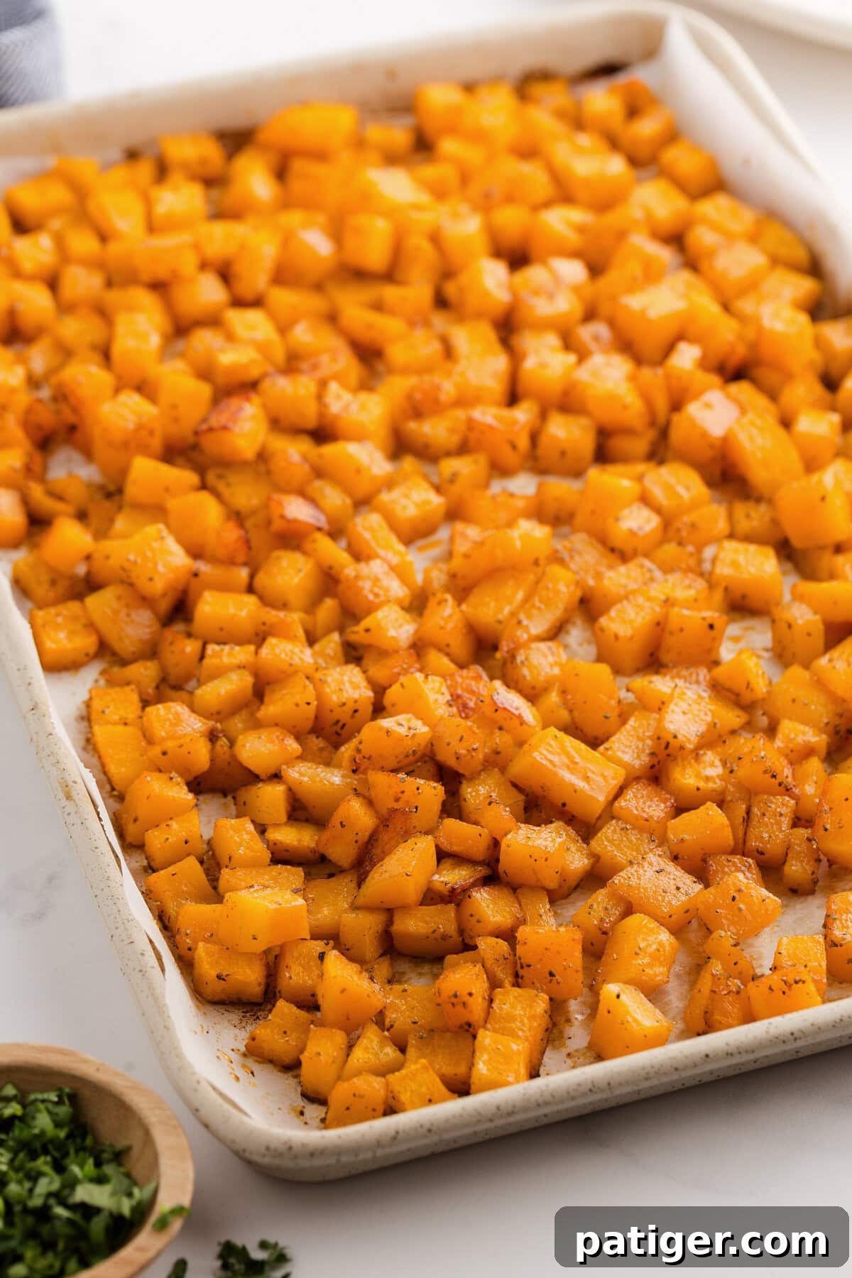 Oven roasted butternut squash spread across a lined baking sheet, showing golden-brown edges.