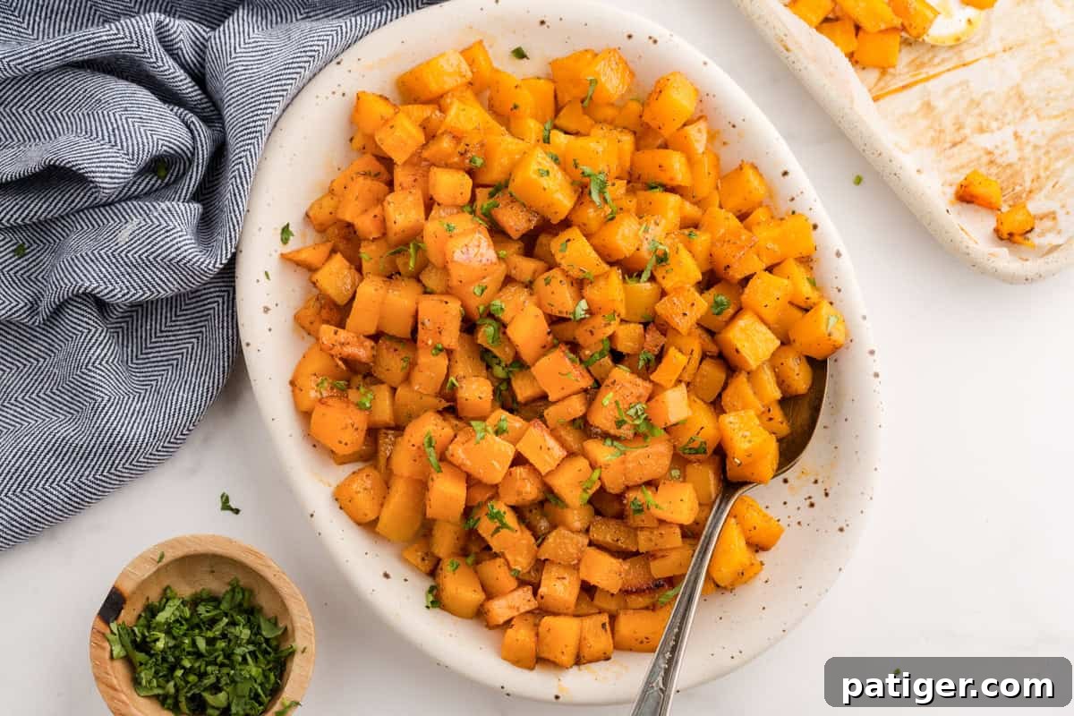 Cubed Roasted butternut squash in a white serving dish with a spoon, ready to be enjoyed.