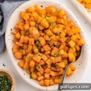 Roasted butternut squash cubes in a white serving dish with a spoon.