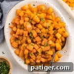 Roasted butternut squash cubes in a white serving dish with a spoon.