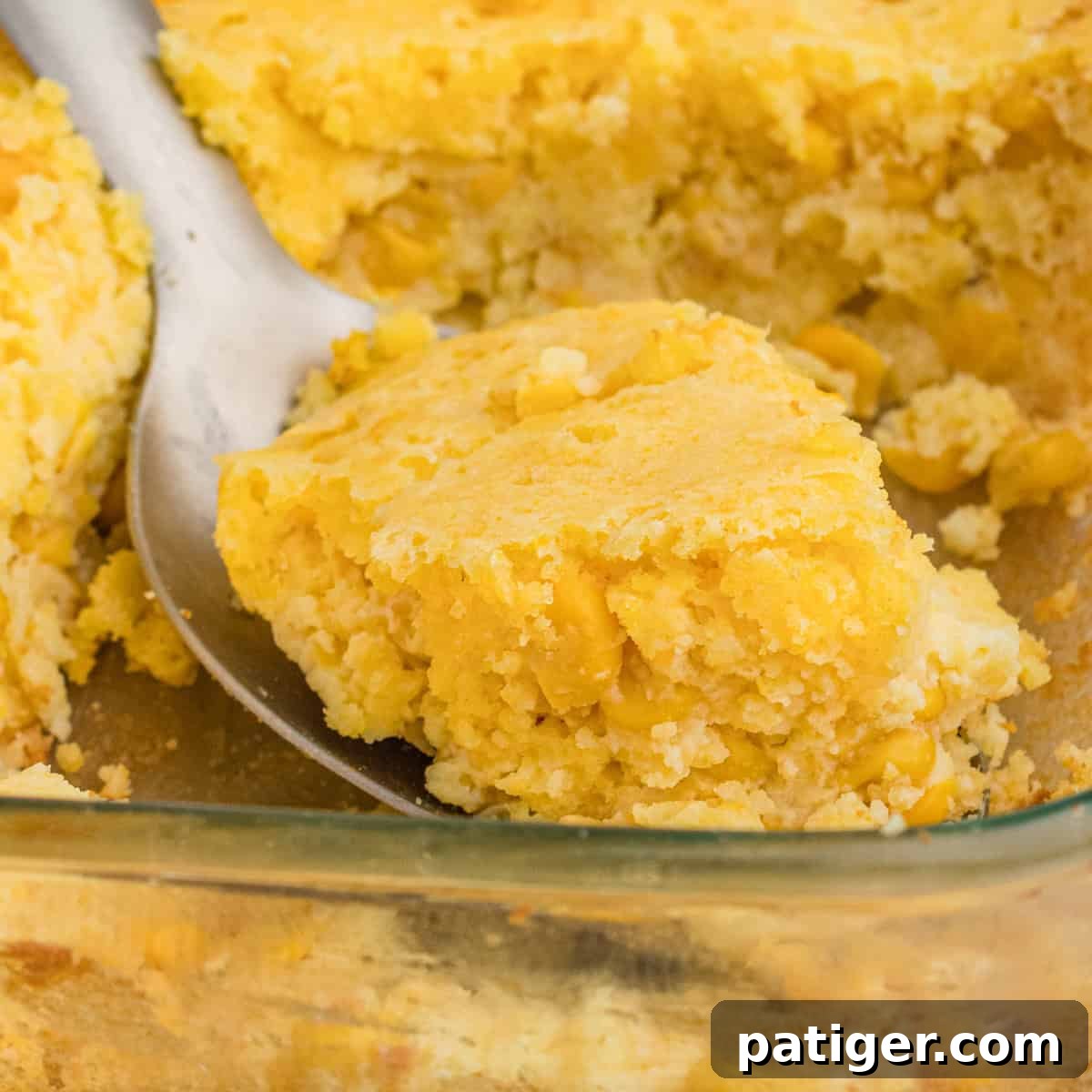 Serving spoon scooping cornbread casserole with jiffy mix and creamed corn.