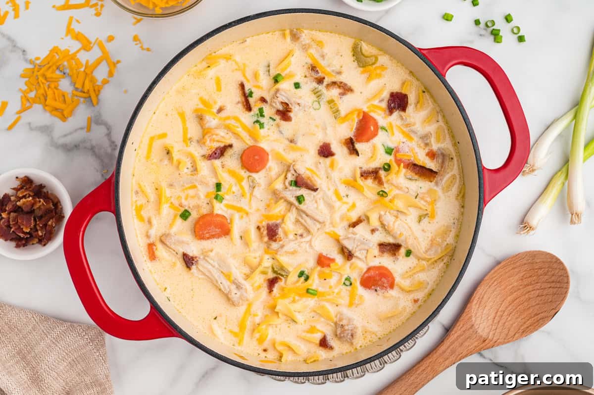 Top-down view of crack chicken noodle soup with egg noodles, bacon and cheese in a red pot.