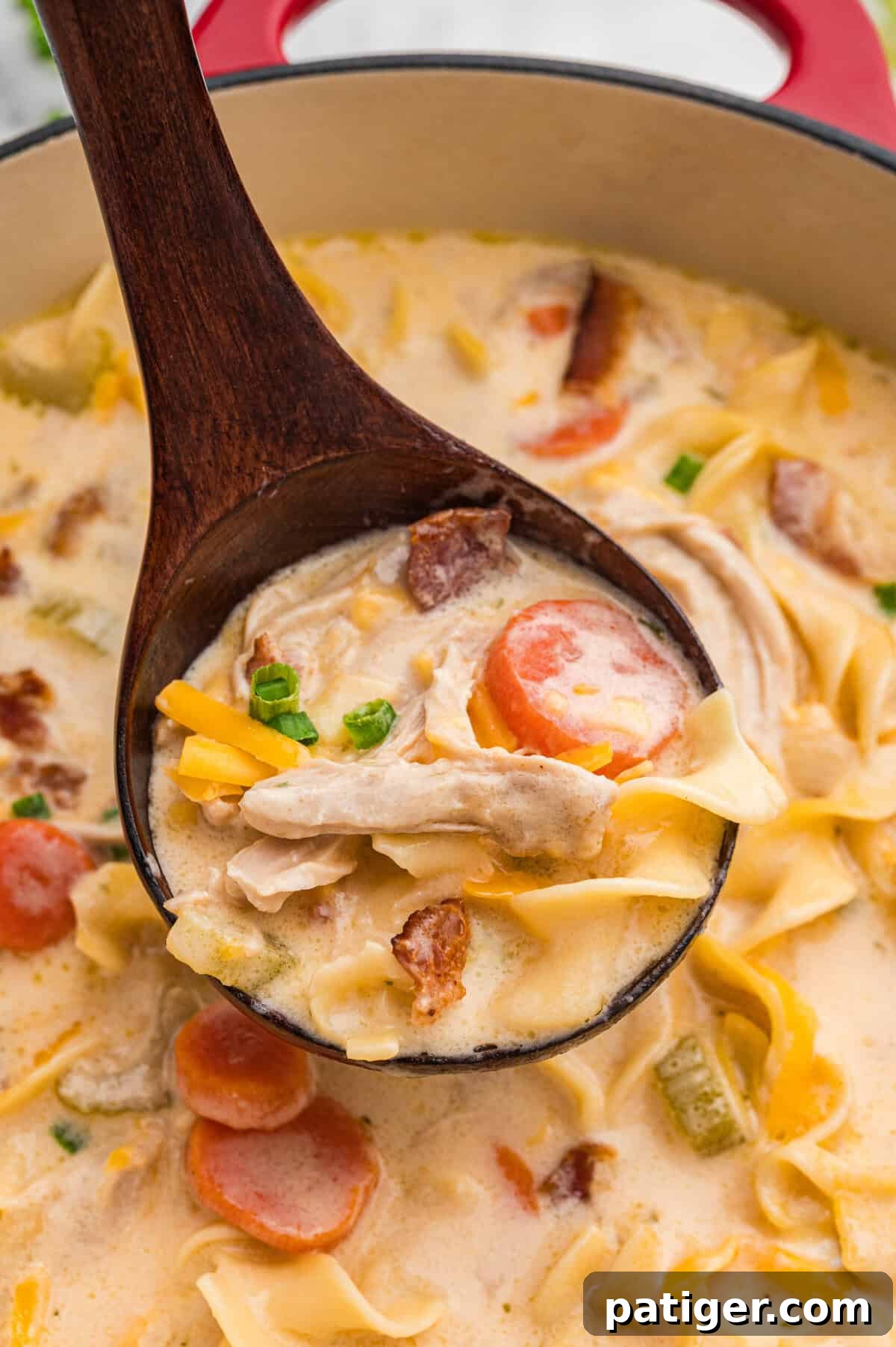 Wooden ladle lifting creamy crack chicken noodle soup from pot.