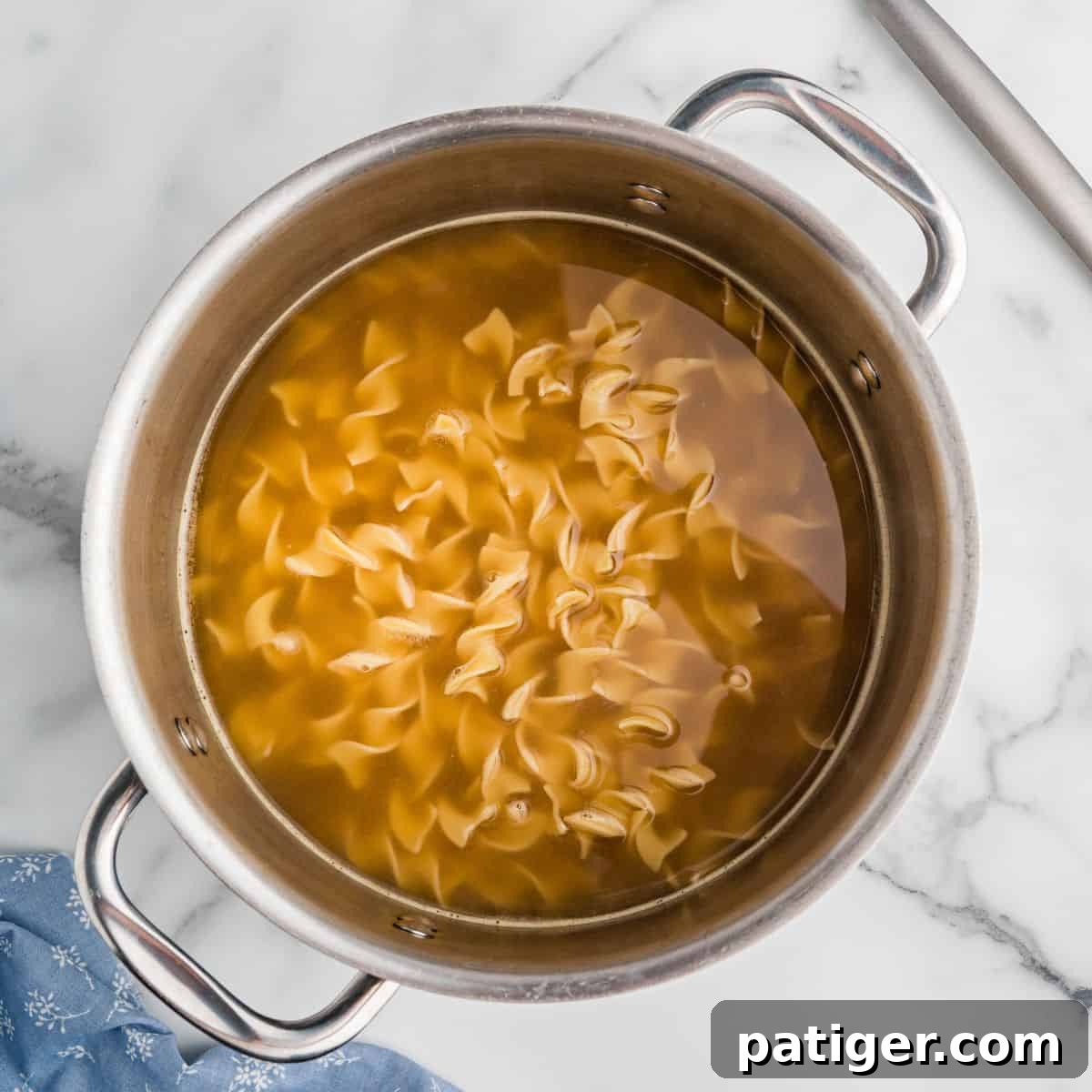 Egg noodles cooking in broth in a stainless steel pot.