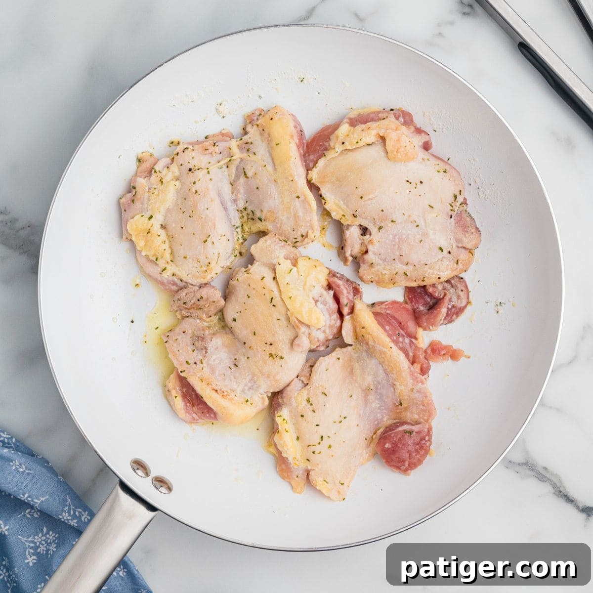Raw chicken thighs seasoned in a white skillet.