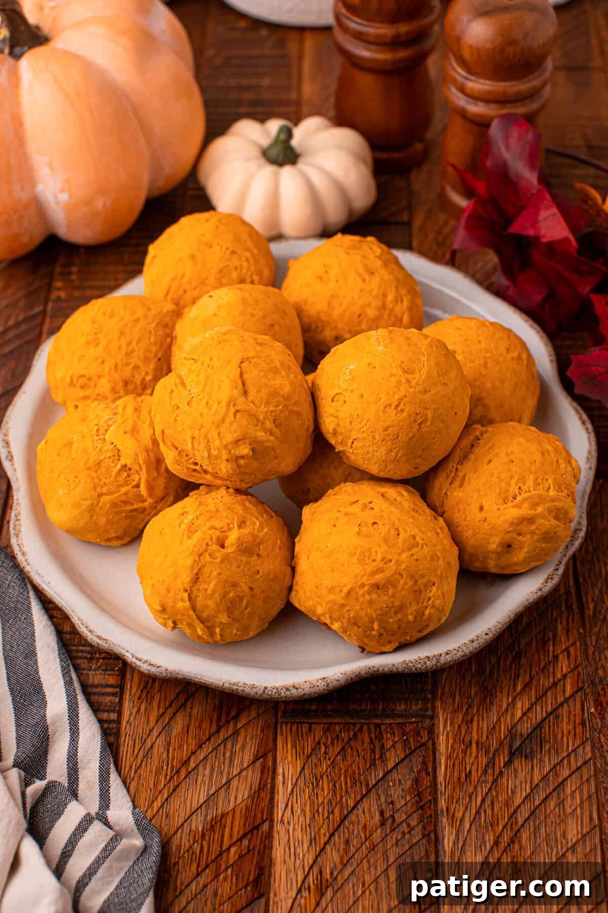A trio of soft, golden pumpkin dinner rolls artfully arranged on a rustic wooden board, with autumn leaves and a cozy fall decor in the soft-focused background, inviting you to the warmth of the season.