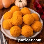 A rustic shot of two soft, golden 2-ingredient pumpkin bread rolls nestled in a bowl, with a scattering of autumn leaves and gourds in the background, evoking a warm fall ambiance.