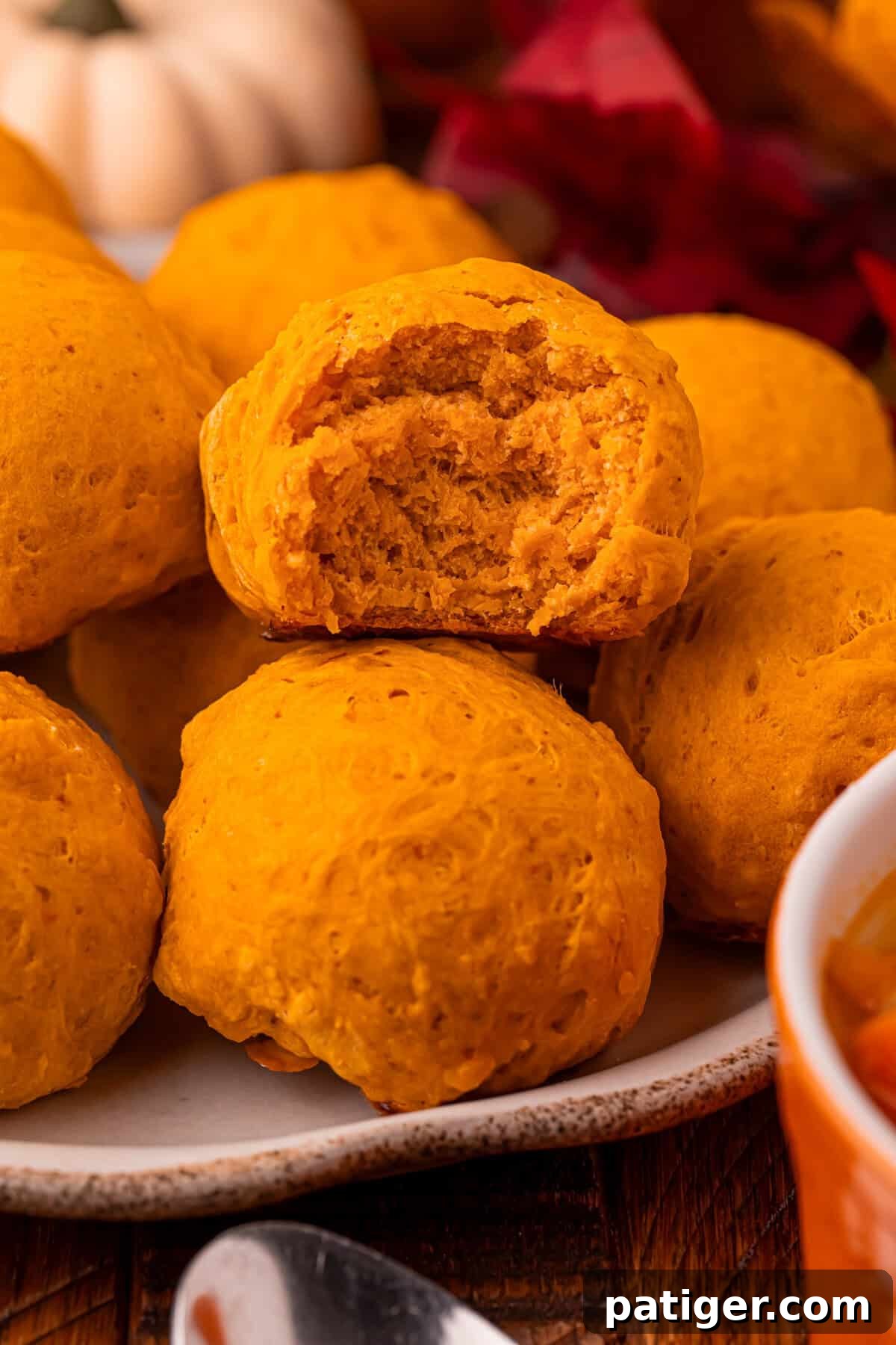 A charming arrangement of pumpkin bread rolls on a plate, with one roll prominently displayed in the foreground, cut open to reveal its moist, soft, and inviting interior.