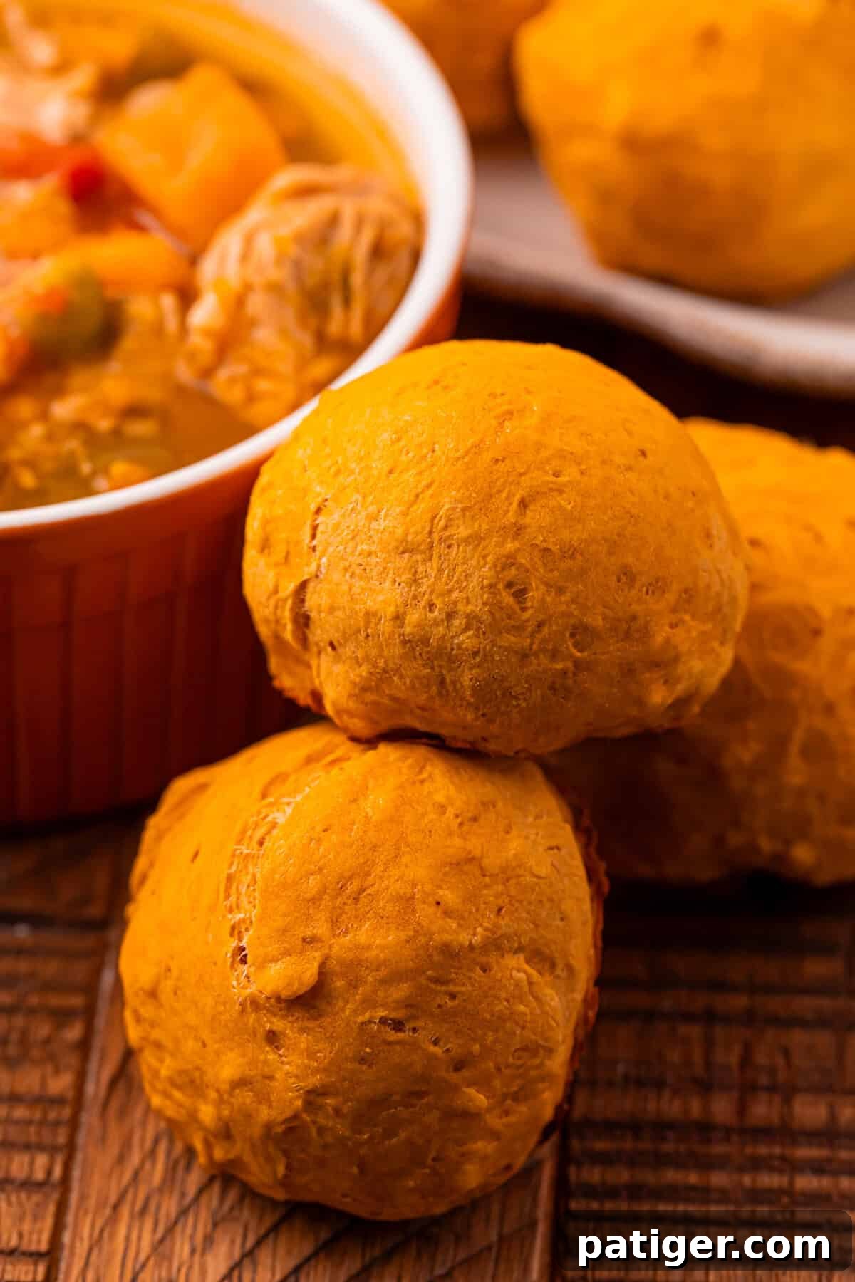 A warm and comforting scene: a plate of freshly baked pumpkin dinner rolls positioned next to a steaming bowl of savory soup, creating a perfect autumn meal.