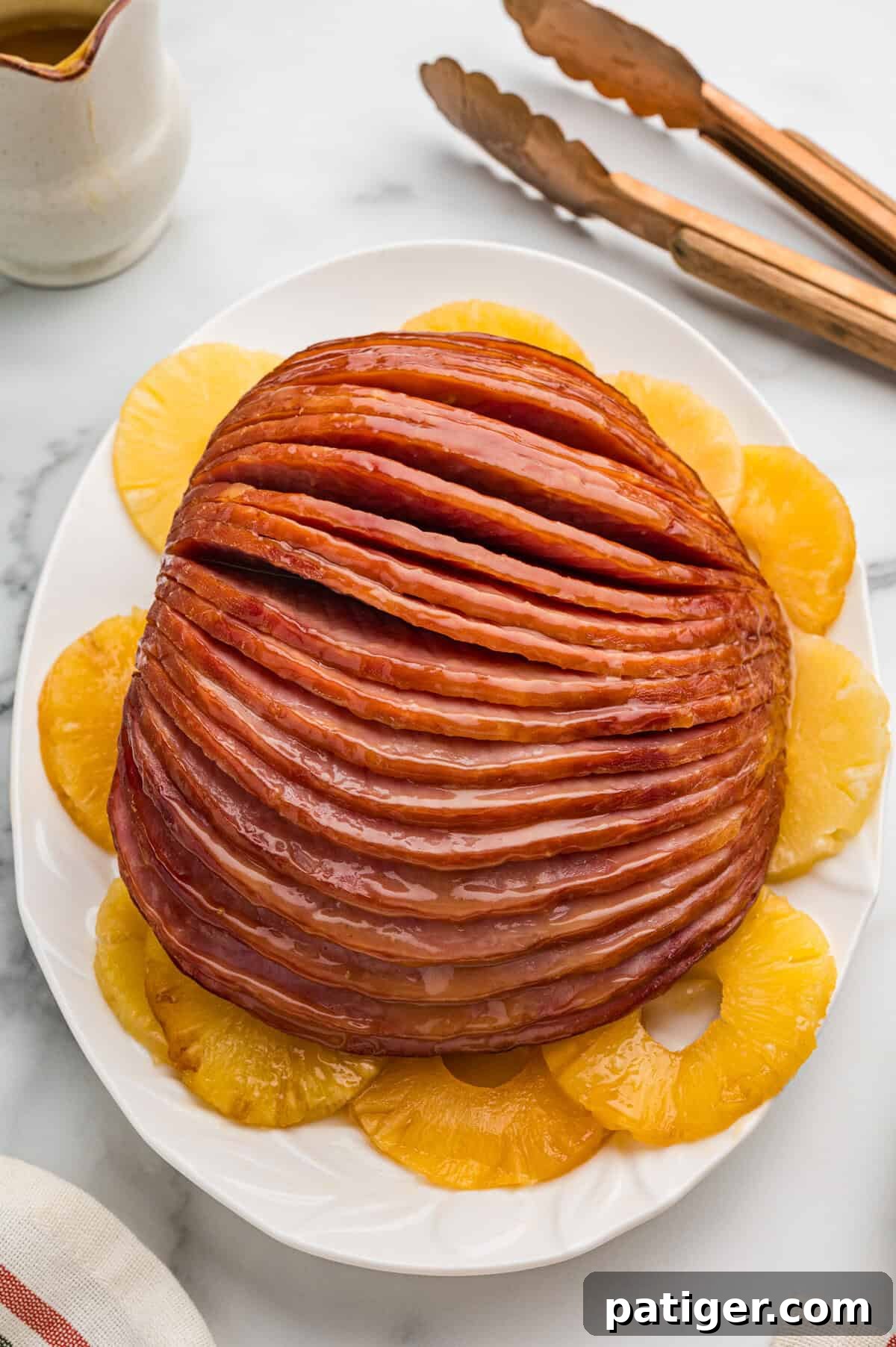 Irresistible Slow Cooker Ham with Pineapple Brown Sugar Glaze 9 A magnificent whole glazed spiral sliced slow cooker brown sugar pineapple ham, elegantly presented on a pristine white platter, artfully encircled by golden pineapple rings. The glaze gives it a beautiful, inviting sheen.