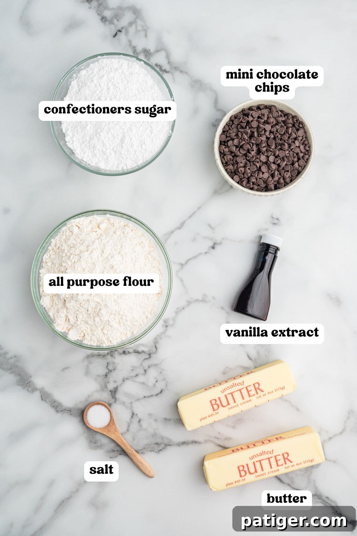 Decadent Chocolate Chip Snowball Bites 4 Overhead image of labeled baking ingredients including a bowl of confectioners sugar, a bowl of mini chocolate chips, a bowl of all-purpose flour, a bottle of vanilla extract, a spoonful of salt, and two sticks of unsalted butter.
