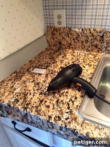 A blow dryer being used on a countertop to help smooth and mold peel and stick granite film around edges and corners.